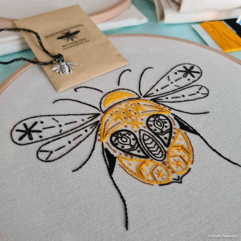Detail view of paisley bee embroidery on white fabric with charity accessories