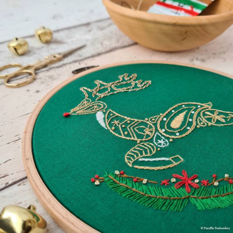 Detail view of reindeer embroidery on green fabric in wooden hoop
