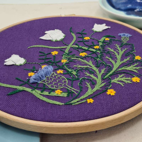 Close up angled shot of botanicals embroidery on purple fabric