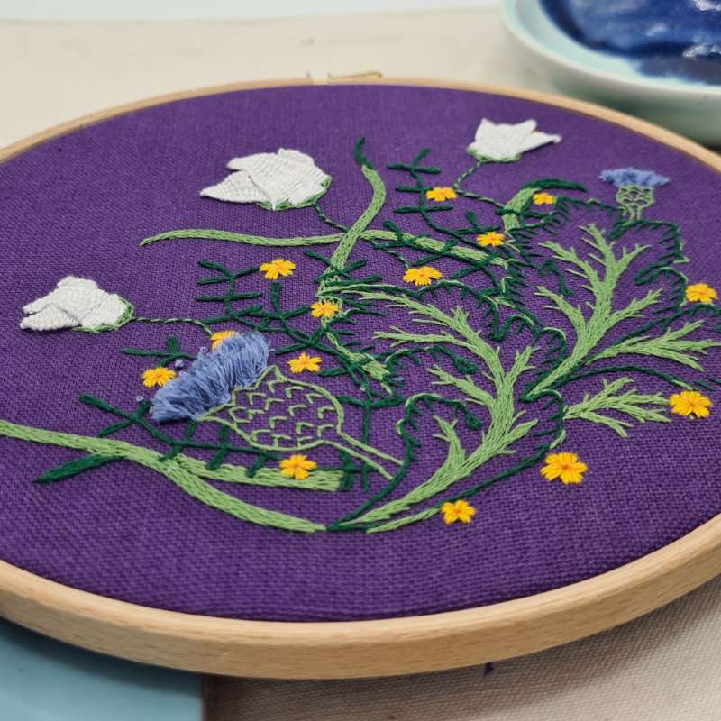 Close up angled shot of botanicals embroidery on purple fabric