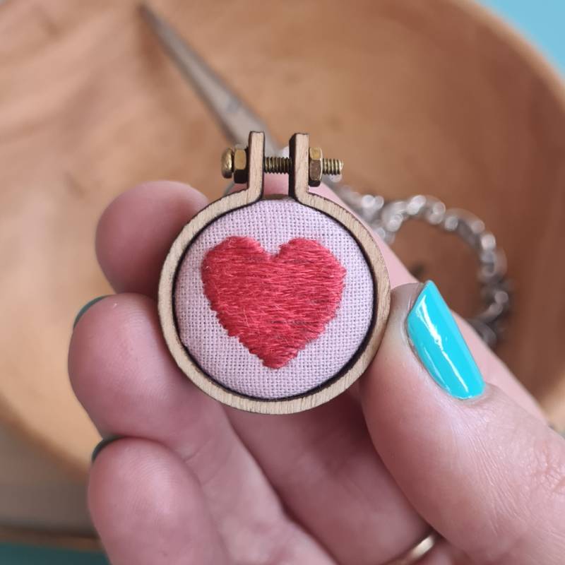 A red heart stitched into pink fabric held in a charm 