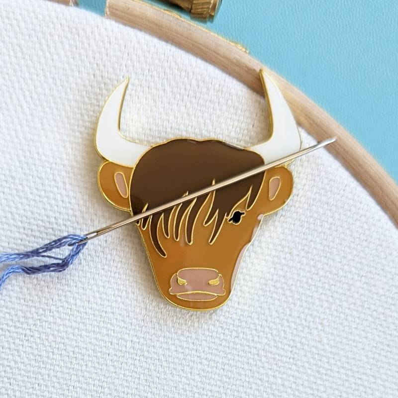 A needle rests on a highland cow shaped magnet, on a white fabric background.