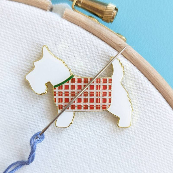 An embroidery needle rests on a magnet with a Scottie Dog with a tartan coat design.