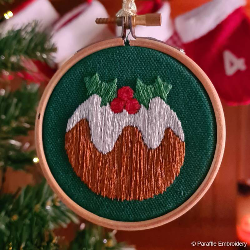 Lifestyle picture of Christmas pudding embroidery on green fabric in wooden hoop