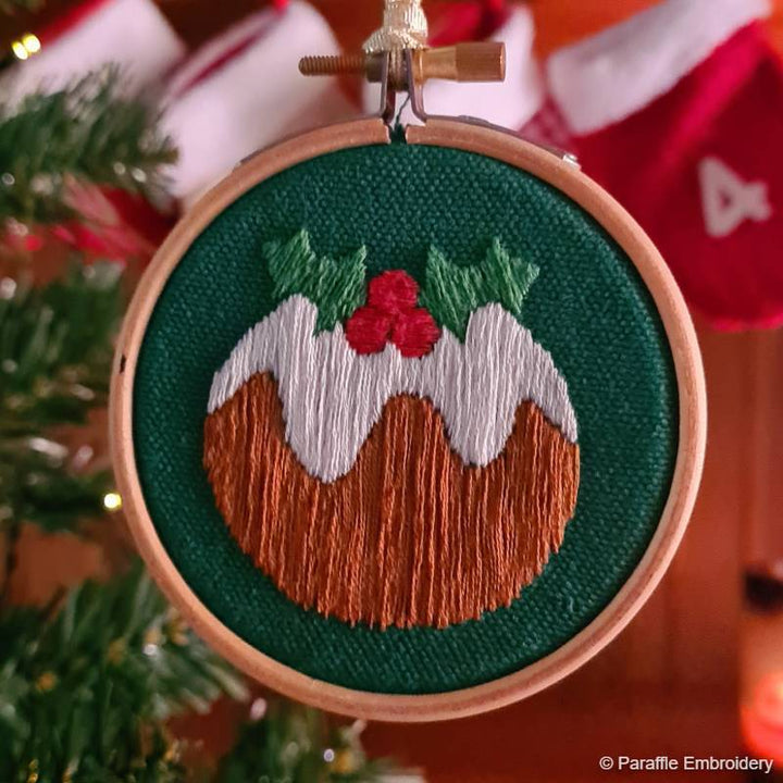 Lifestyle picture of Christmas pudding embroidery on green fabric in wooden hoop