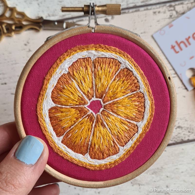 Lifestyle view of Orange needle painting embroidery on pink fabric in wooden hoop