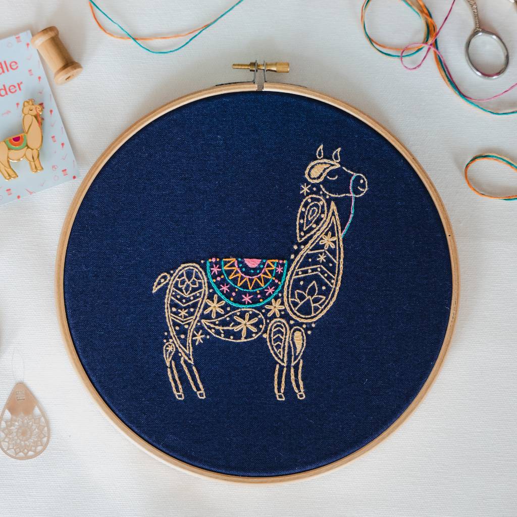 An embroidery hoop containing navy fabric, stitched with a paisley Llama design.