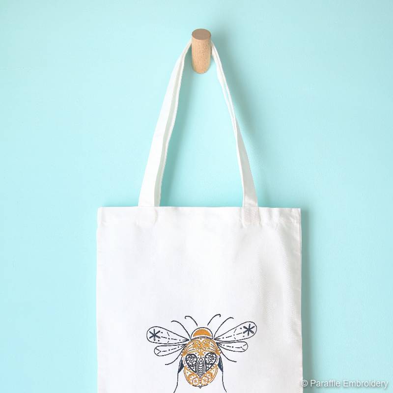 Lifestyle view of paisley bee tote embroidery kit hanging on a hook