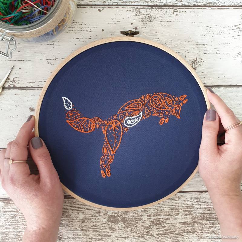 Detail view of paisley fox hand embroidery on navy fabric