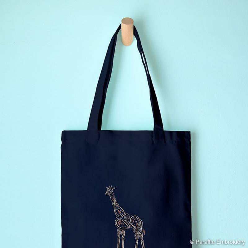 Lifestyle view of giraffe embroidery on navy tote hanging on a hook