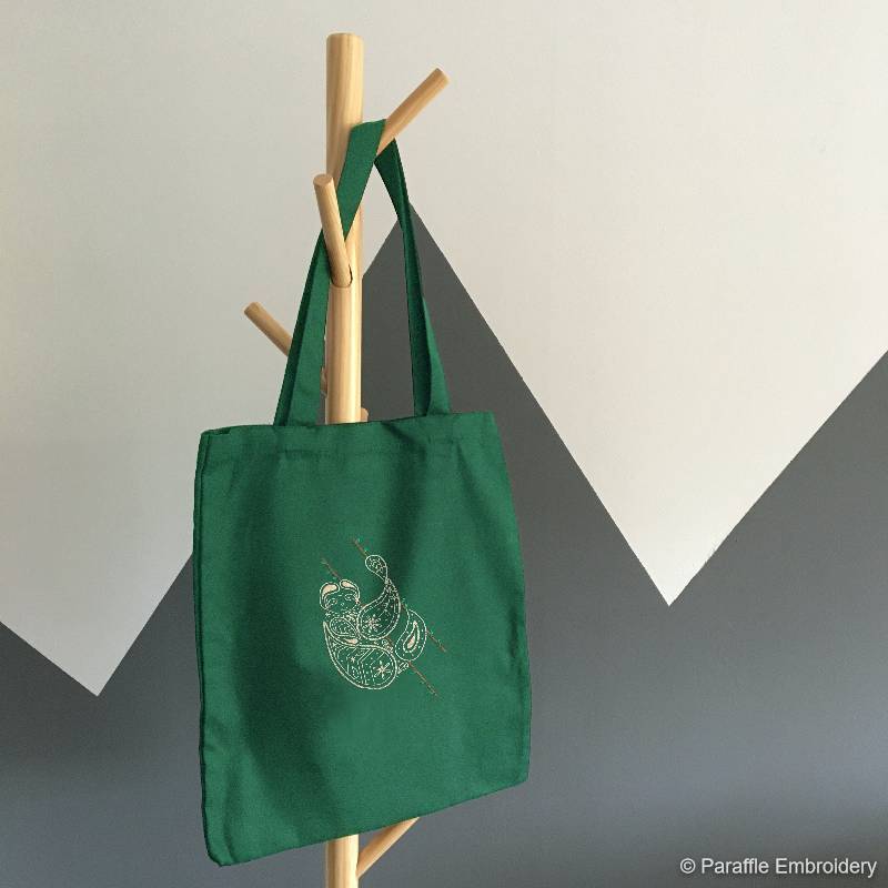 Picture of sloth embroidery on green tote fabric displayed on a coat stand