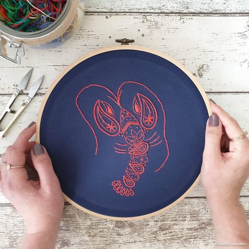 Detail view of paisley lobster hand embroidery on navy fabric