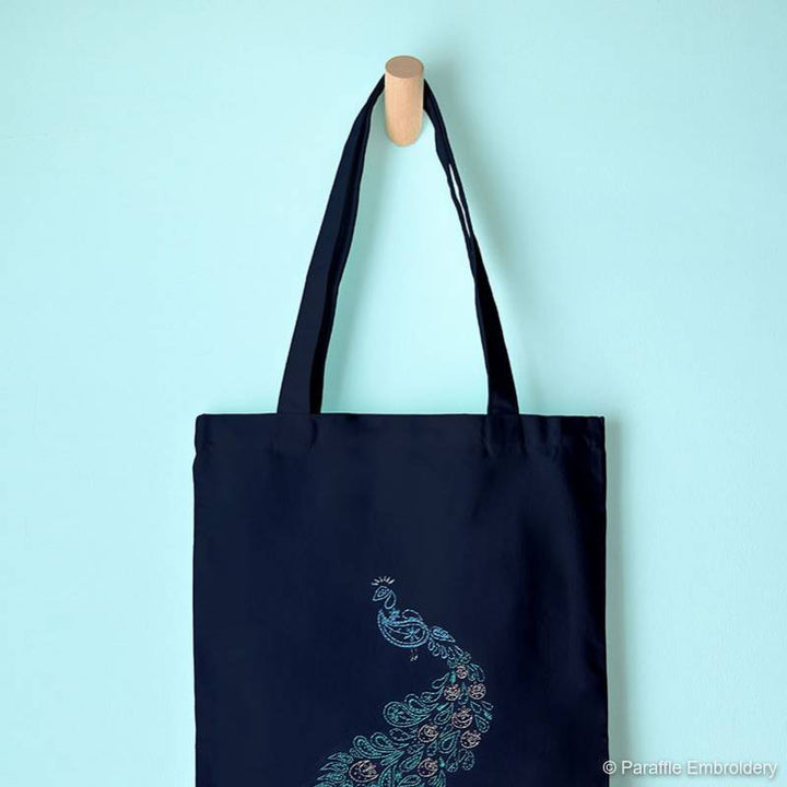 Lifestyle view of paisley peacock embroidery on navy tote hung from display hook