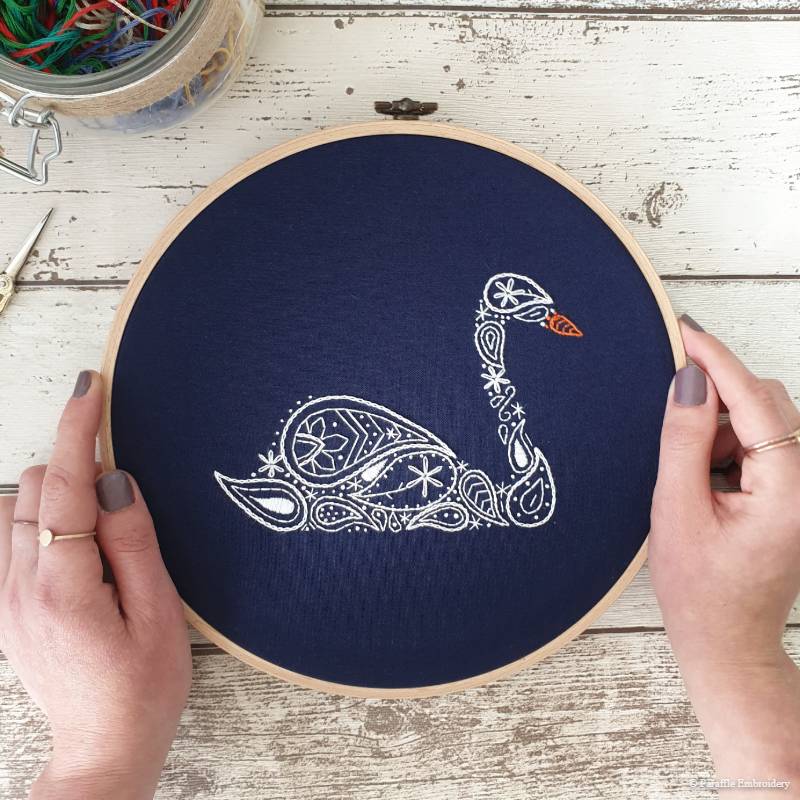 Detail view of paisley swan hand embroidery on navy fabric