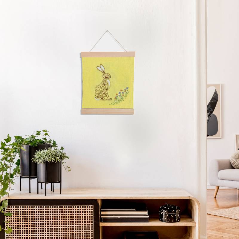 A banner holding yellow fabric set against a white backdrop. The yellow fabric is embroidered with a paisley style rabbit design.