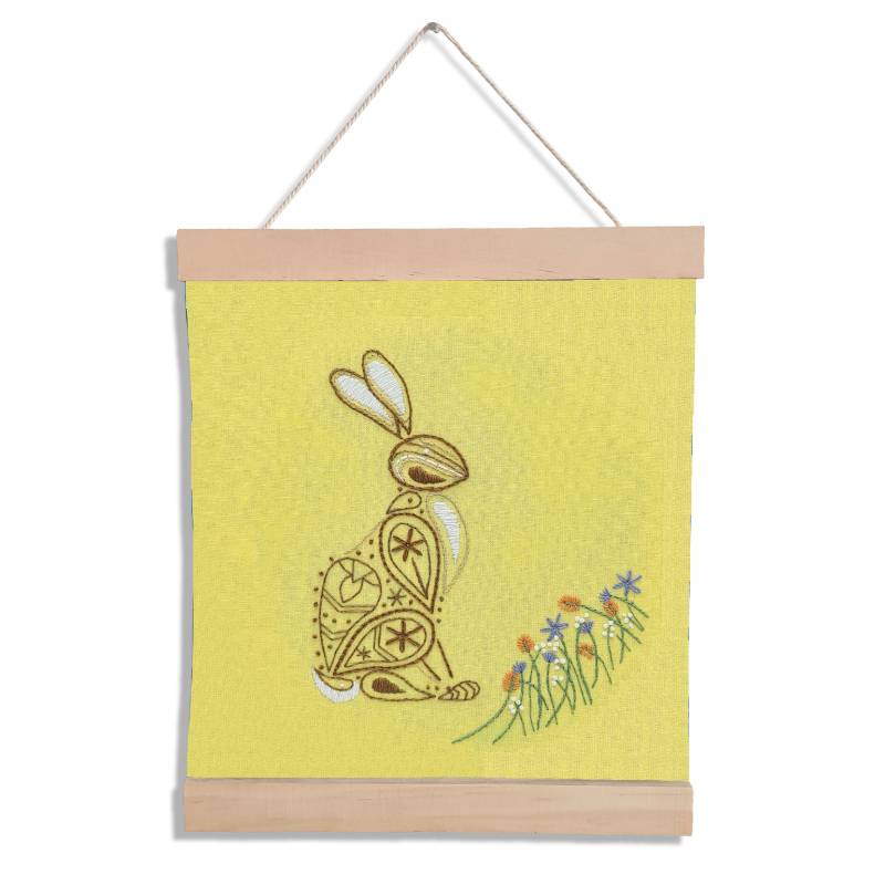 A banner holding yellow fabric set against a white backdrop. The yellow fabric is embroidered with a paisley style rabbit design.