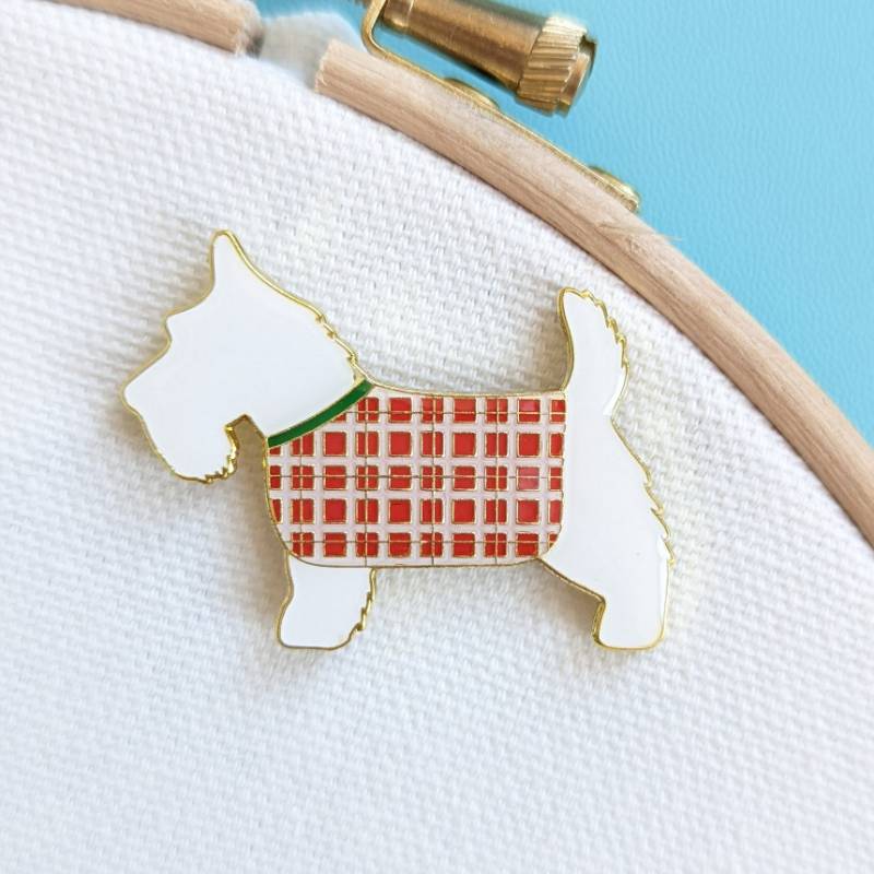 A Scottish Terrier with tartan coat magnet rests on a cream fabric background.