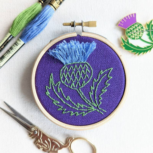 A bird's eye view of a 3 inch embroidery hoop containing purple fabric and stitched with a Scottish thistle design.