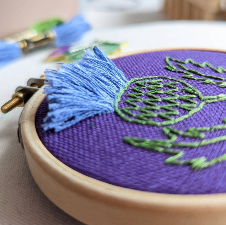 A close up of lilac embroidery thread using Turkey Work stitch on purple fabric.