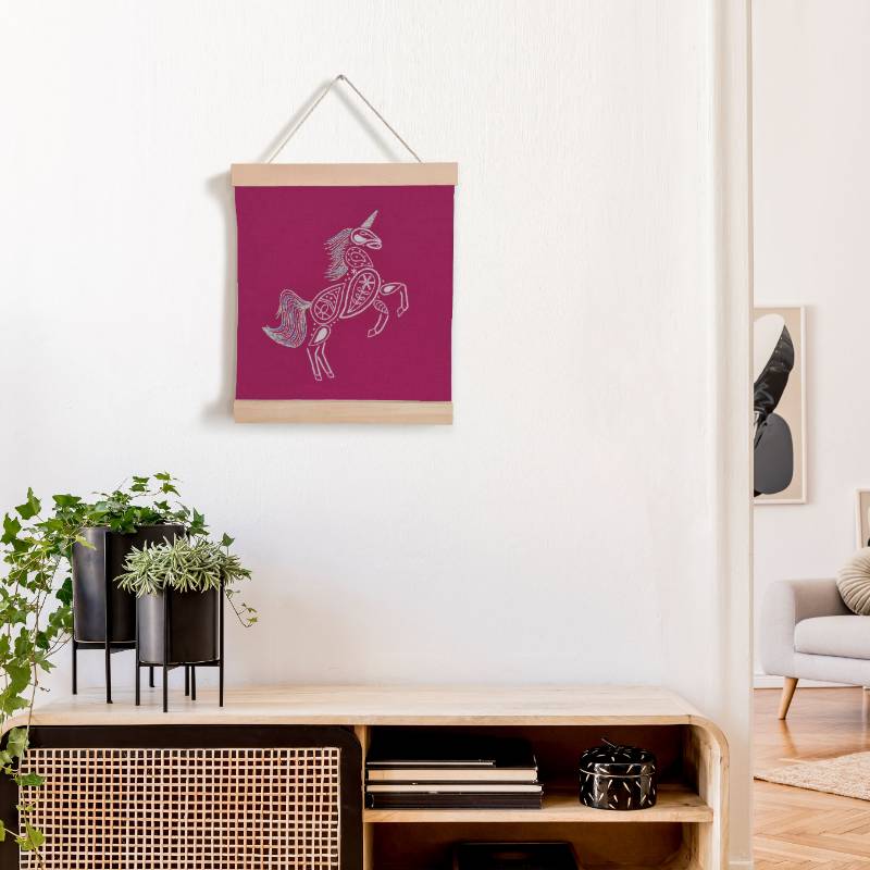A wooden banner holding a piece of bright pink fabric, against a white background. The fabric is embroidered with a white unicorn design.