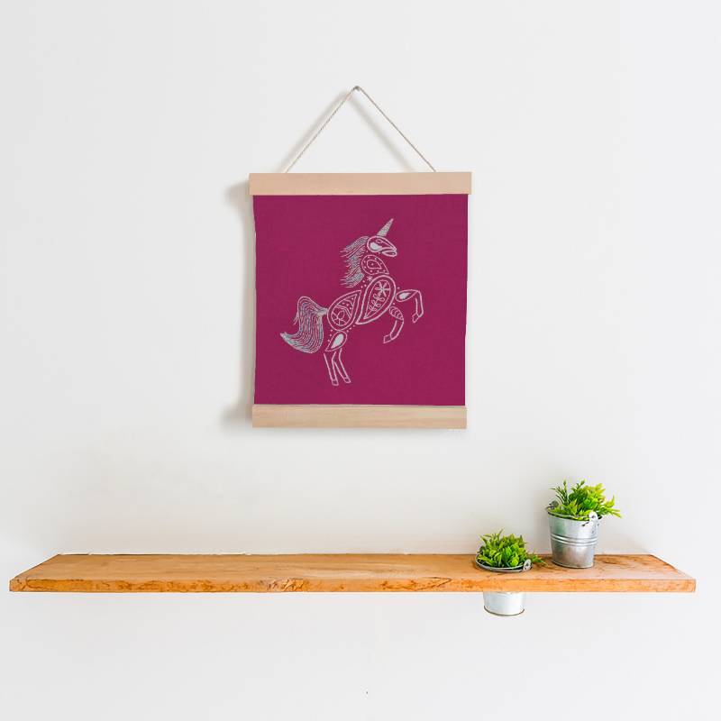 A wooden banner holding a piece of bright pink fabric, against a white background. The fabric is embroidered with a white unicorn design.