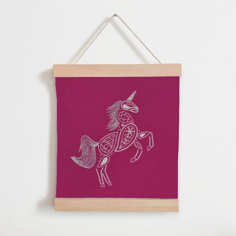 A wooden banner holding a piece of bright pink fabric, against a white background. The fabric is embroidered with a white unicorn design.